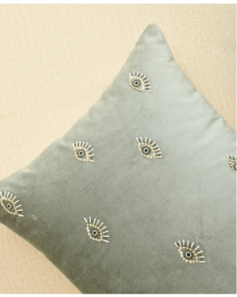 Hand-embroidered evil eye cushion cover on mint green velvet, adding elegance and protection to any space.