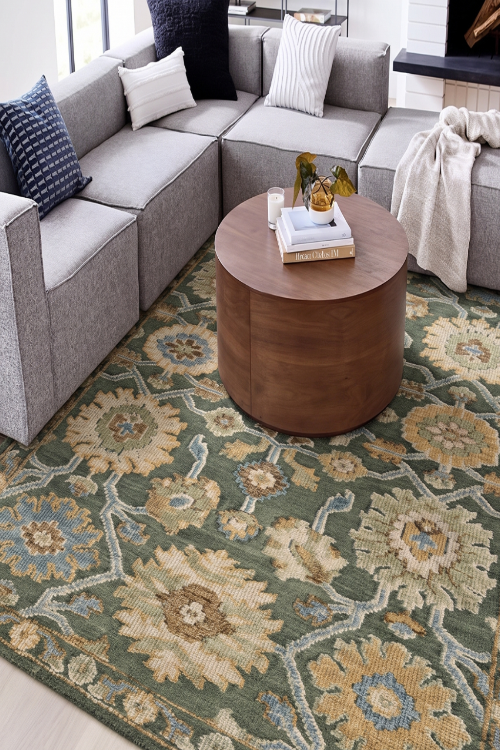 Living room with a gray sectional sofa, round wooden coffee table, and patterned rug.