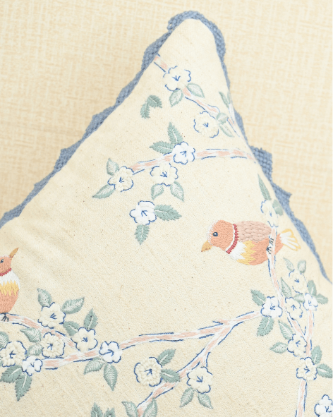 Close-up of a Hummingbirds cushion cover featuring embroidered birds and blue lace trim.