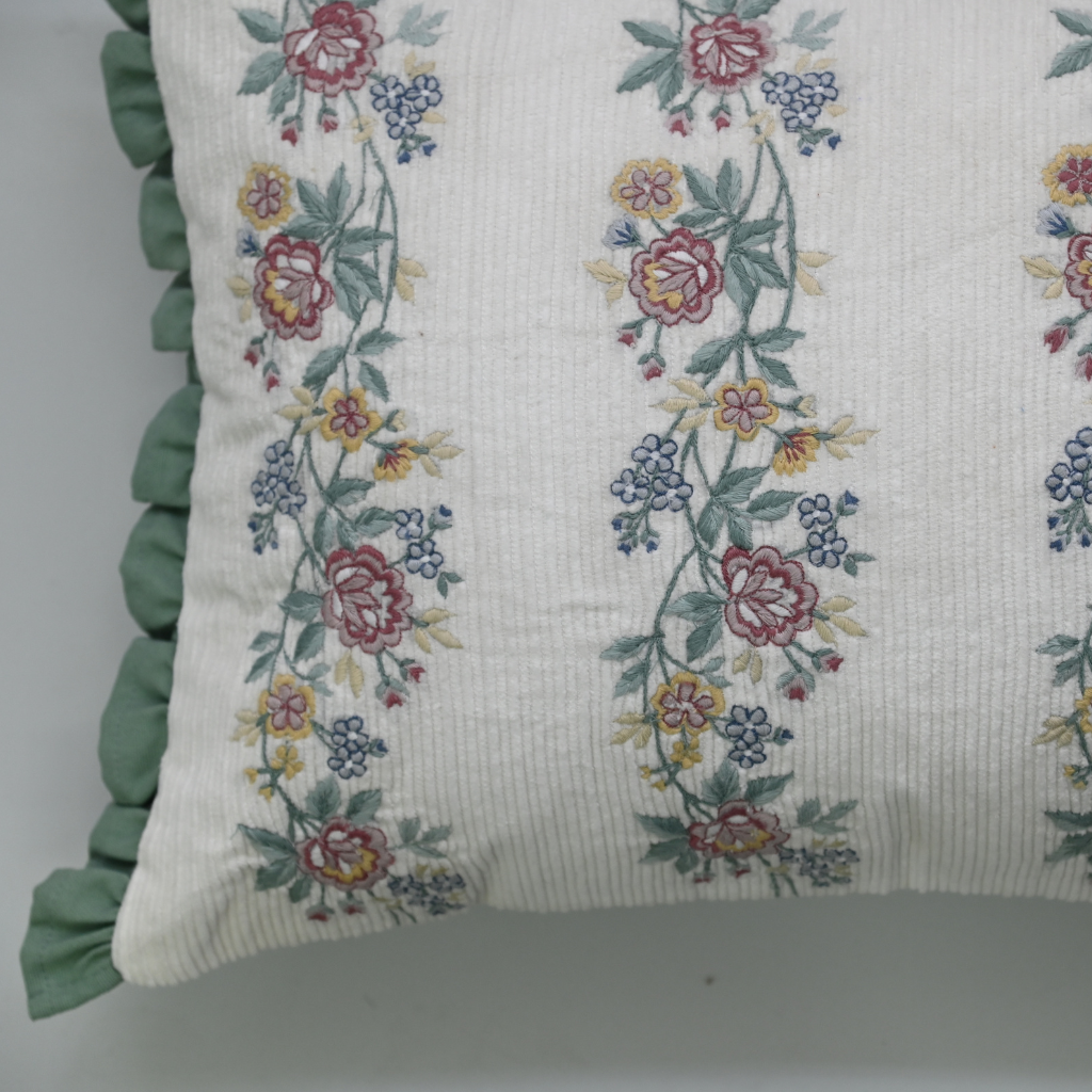 Floral embroidered pillow with green ruffle on a plain background