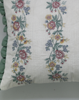 Floral embroidered pillow with green ruffle on a plain background