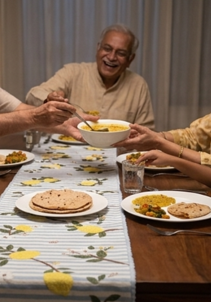 Family gathered around a dining table for a meal, with plates of food and a smiling elderly man.