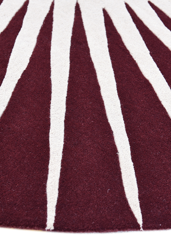 Sun inspired round wool rug featuring bold white rays on maroon background