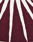 Sun inspired round wool rug featuring bold white rays on maroon background